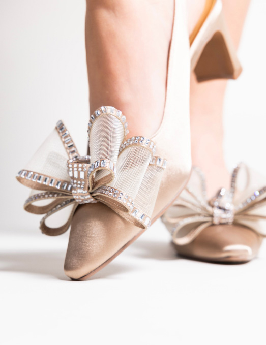 close-up of a satin beige special occasion shoe with a mesh and rhinestone bow ornament on a woman's foot